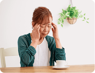 こめかみを両手で押さえて頭痛に悩む女性